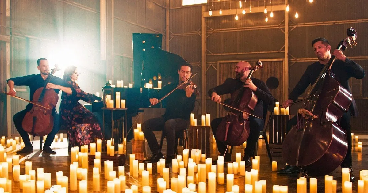 A string quartet performs surrounded by candles in a dimly lit, rustic setting.