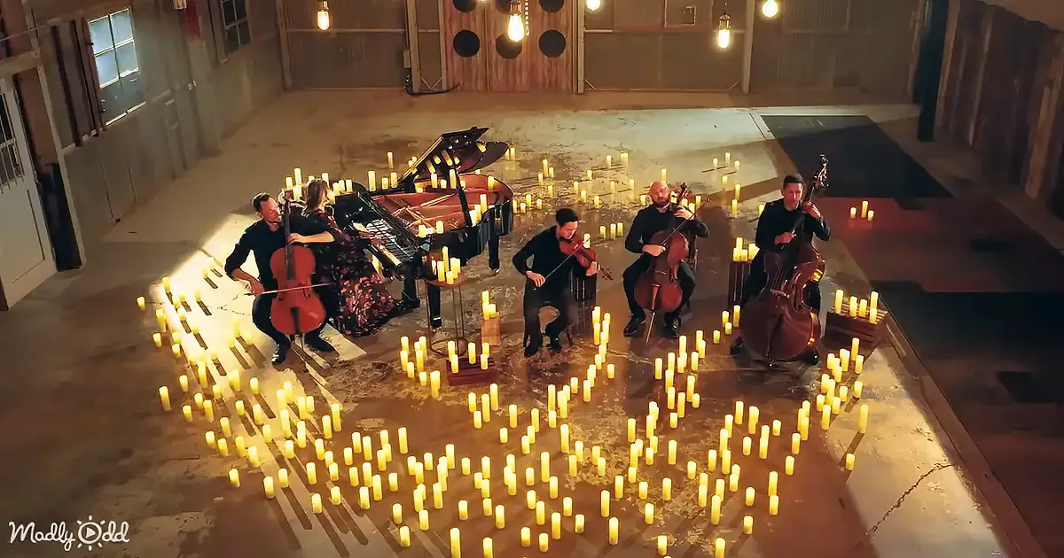A string quartet and a pianist perform surrounded by candles in a dimly lit room.