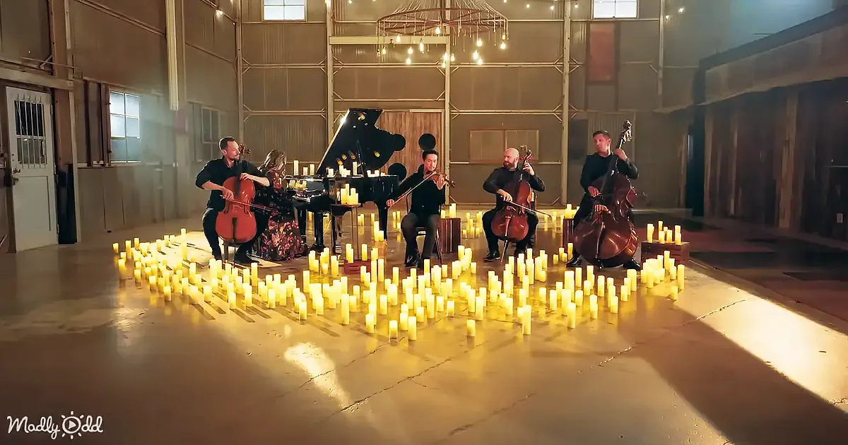 A string quartet and a pianist perform surrounded by candles in a dimly lit warehouse.