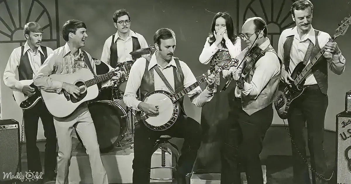 A band performs with a banjo player, guitarists, a violinist, and a singer, all dressed in casual attire.