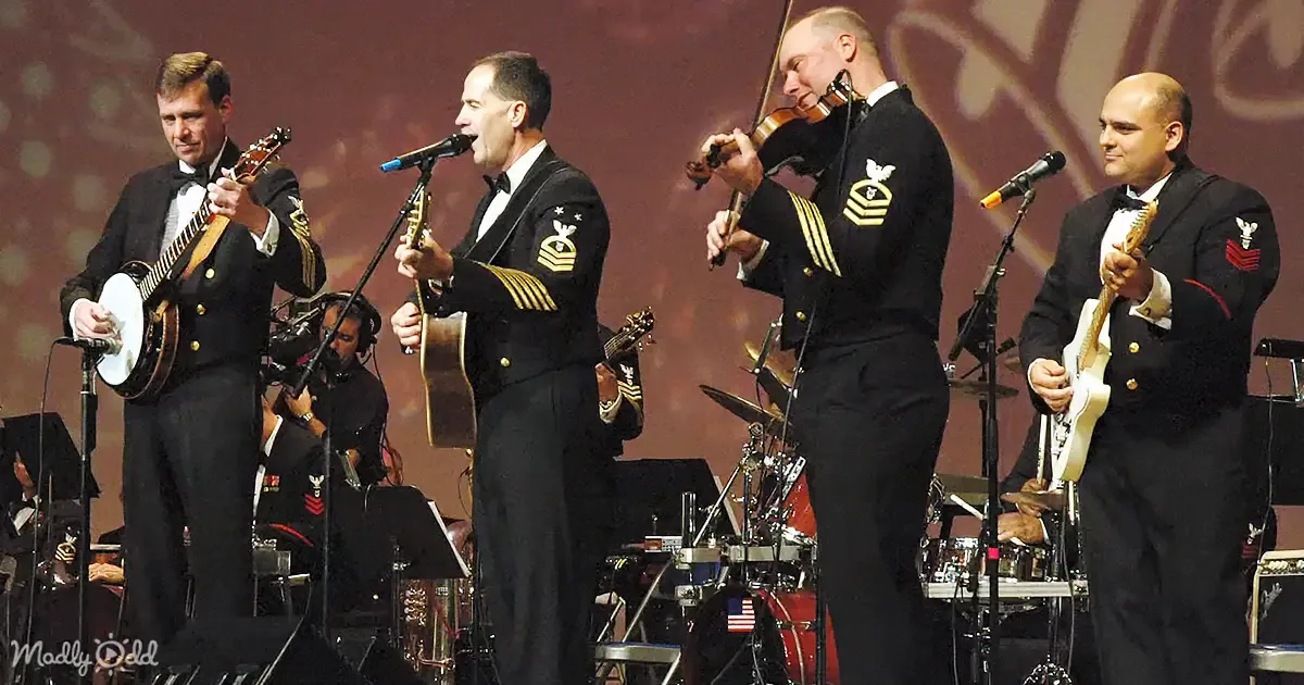 A group of musicians in military uniforms perform on stage, playing banjo, guitar, violin, and singing.