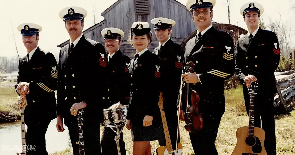 A group of musicians in navy uniforms poses outdoors, holding instruments.
