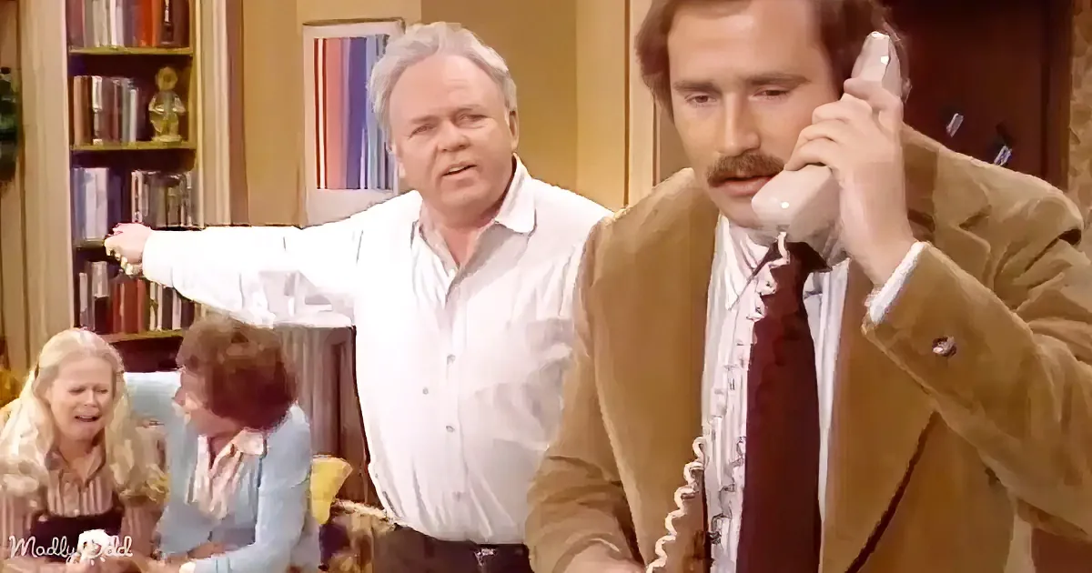 A man in a brown suit holds a phone to his ear, while another man in a white shirt gestures dramatically in the background.
