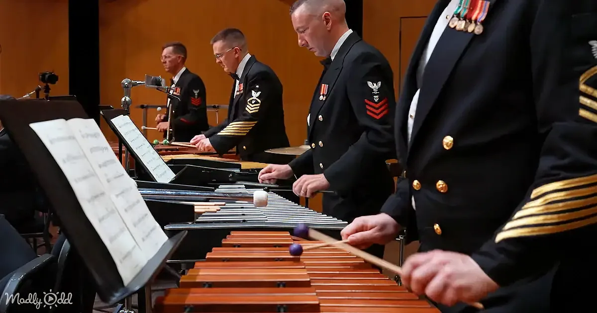 Military musicians in formal uniforms play xylophones in a concert setting.