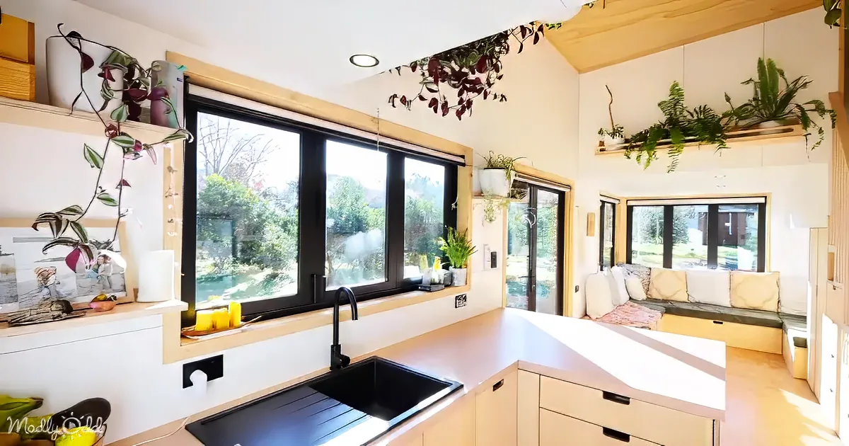 A cozy, sunlit kitchen with a black sink, white cabinets, and a large window overlooking a garden.