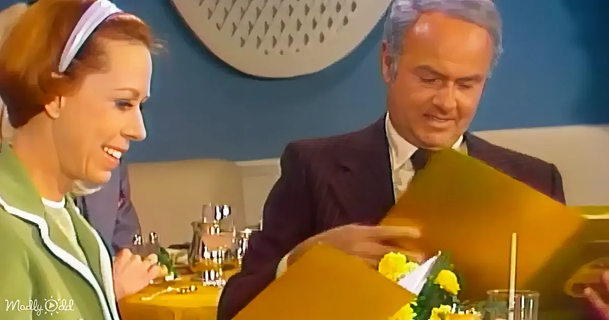 A man in a suit holds a menu while a woman in a green dress smiles beside him at a table.