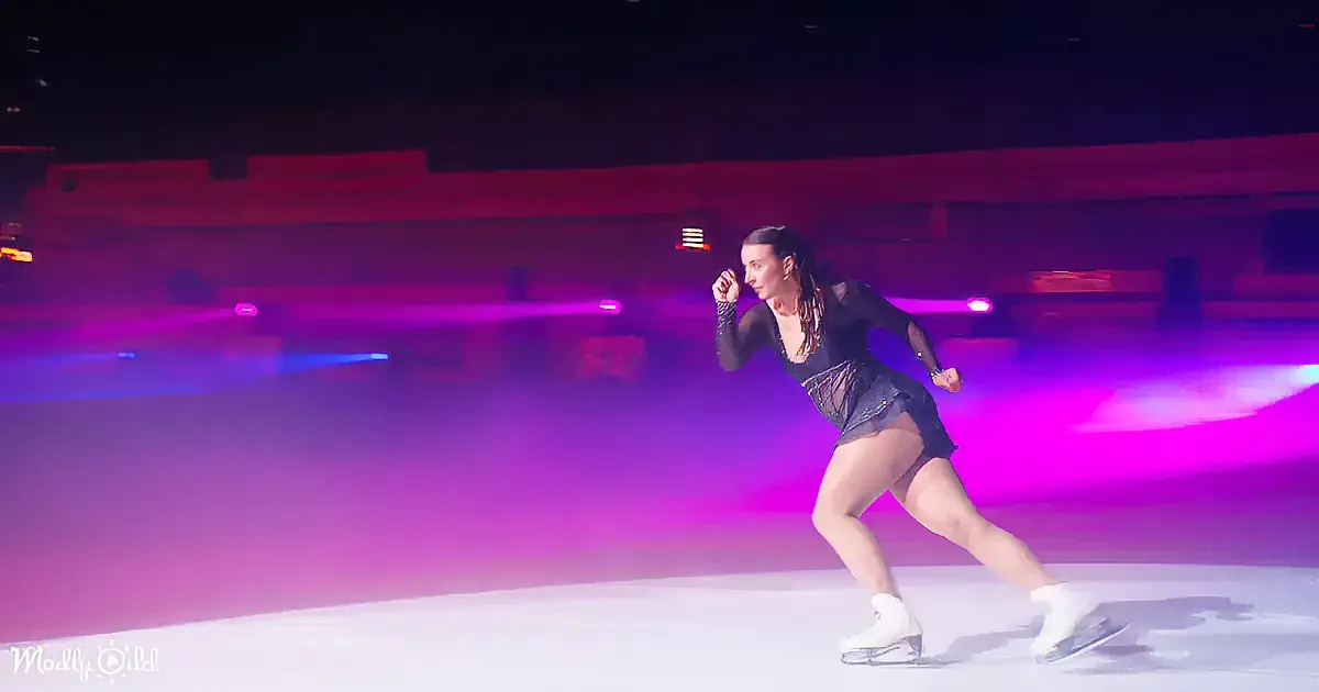 A figure skater in a black outfit glides gracefully on ice, surrounded by vibrant purple and blue lights.