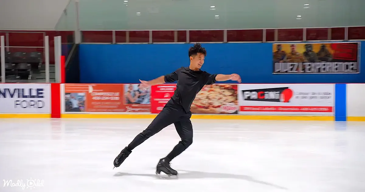A figure skater in black attire glides gracefully on an ice rink, surrounded by advertisements.
