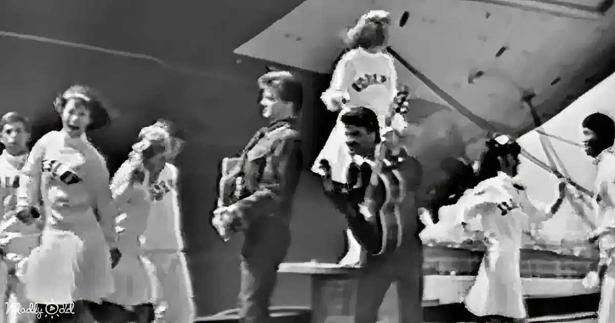 A person in a military uniform stands among a group of people in white uniforms, possibly on a ship.