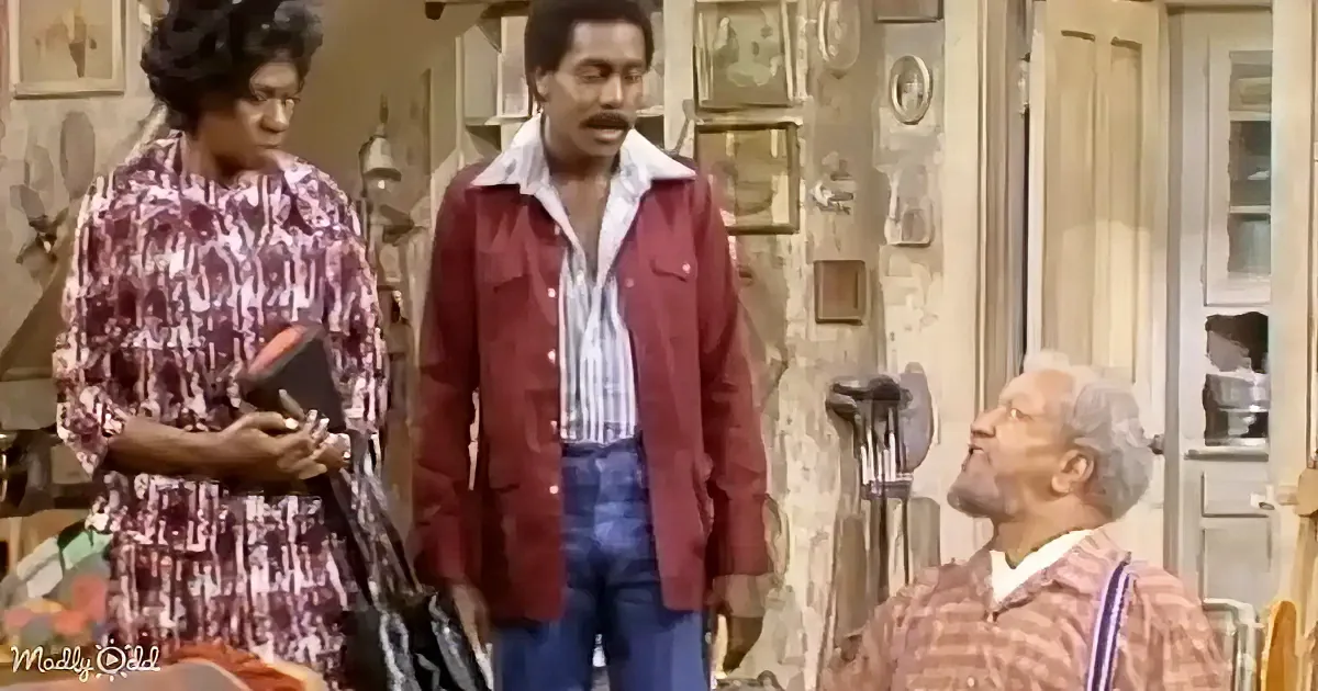 A man in a red jacket stands between a woman in a floral dress and an older man in a plaid shirt, in a room with various...