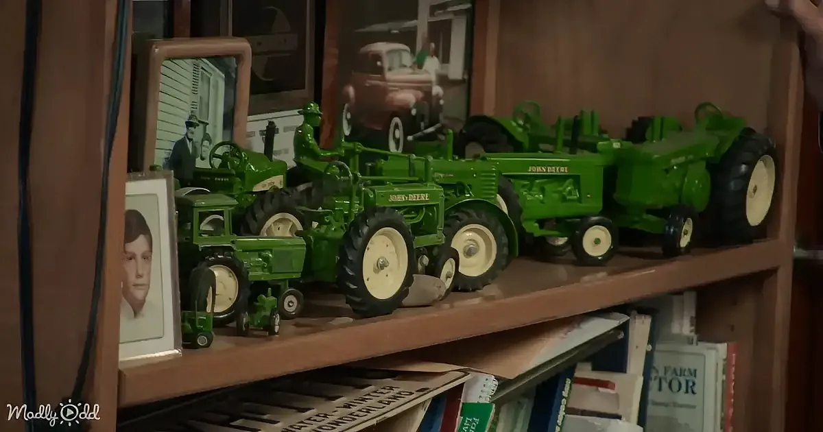 A collection of green John Deere toy tractors displayed on a wooden shelf.