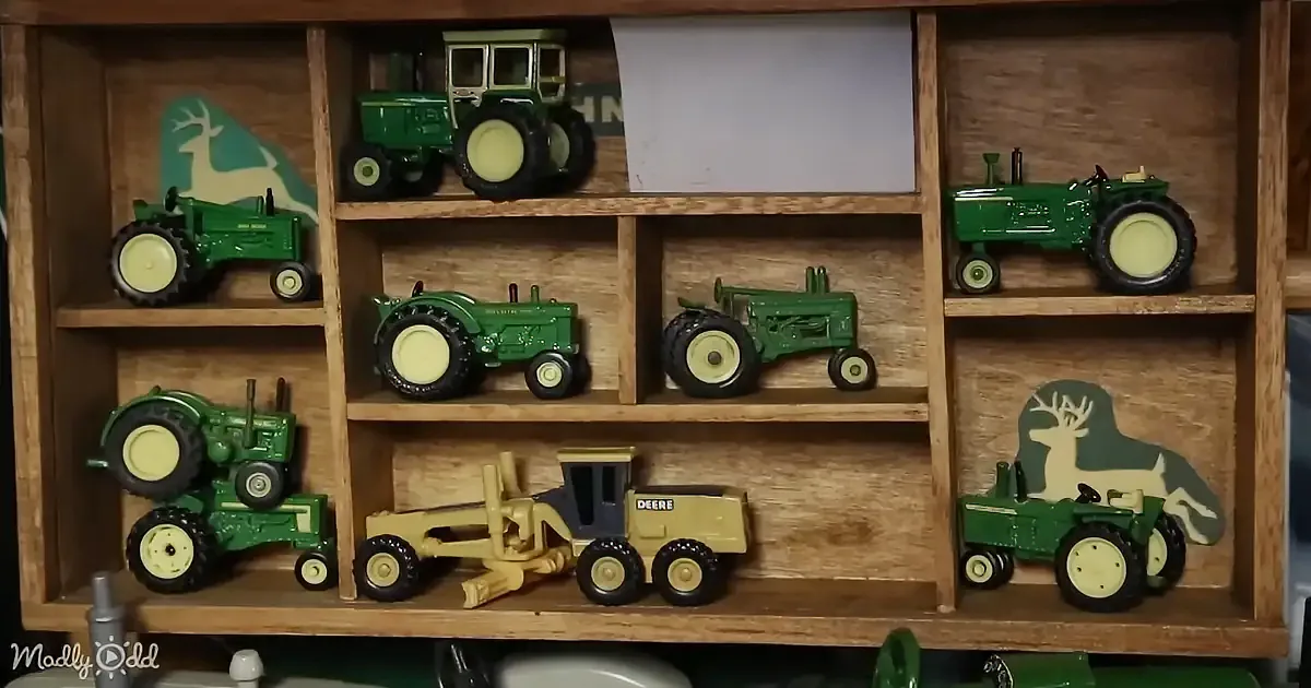 A wooden shelf displays various green toy tractors and a yellow John Deere tractor model.