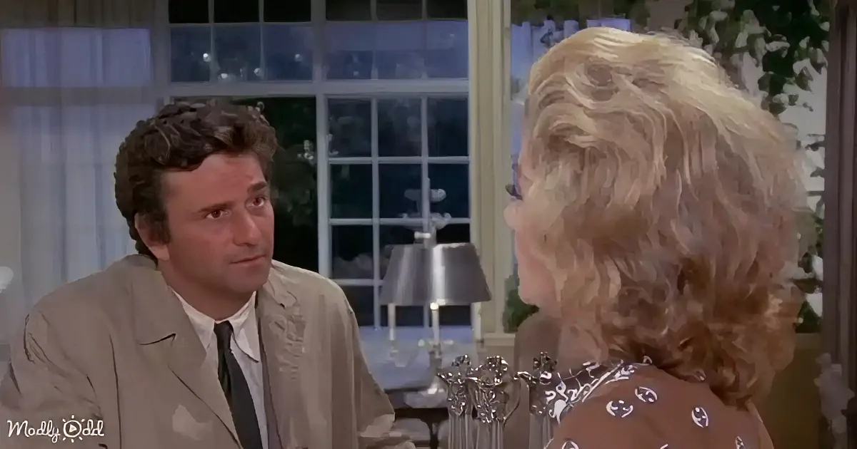 A man in a suit and tie sits across from a woman with blonde hair, both in a room with a lamp and window.