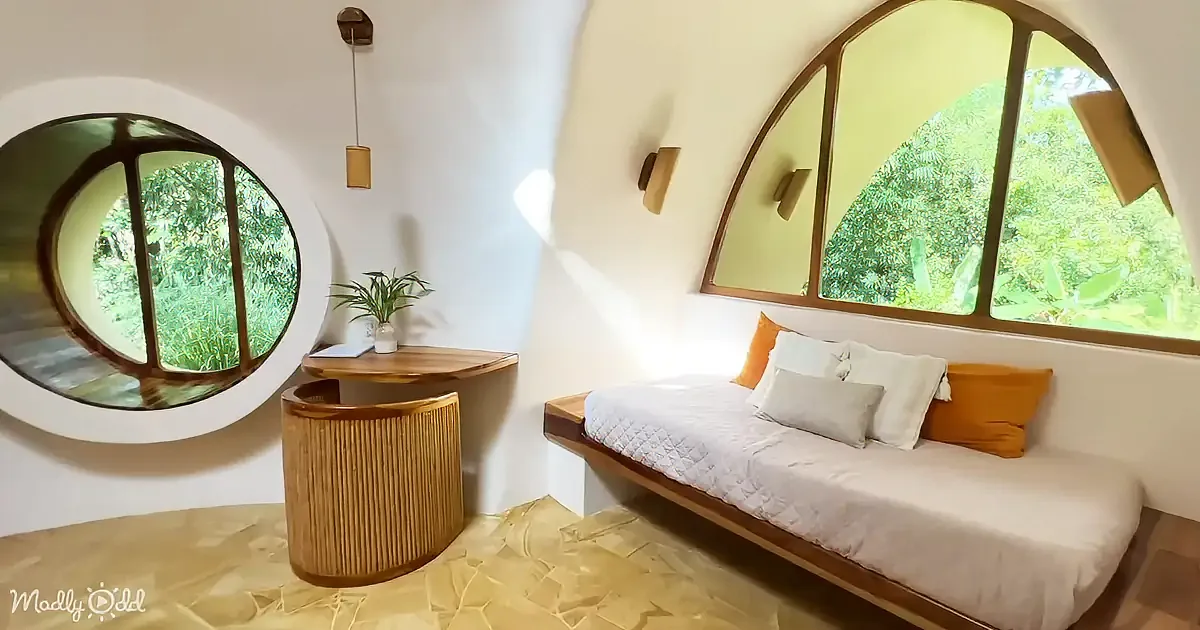 An orange dome-shaped house with a wooden door, surrounded by plants and a stone pathway.
