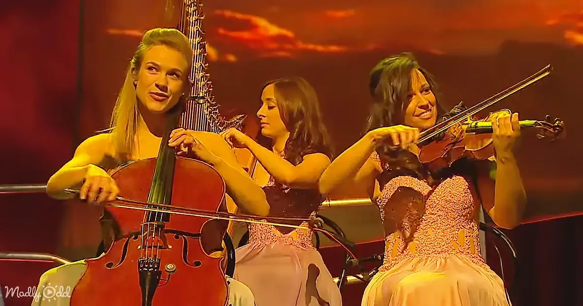Three women play string instruments on stage, one with a cello, another with a violin, and the third with a viola, under...