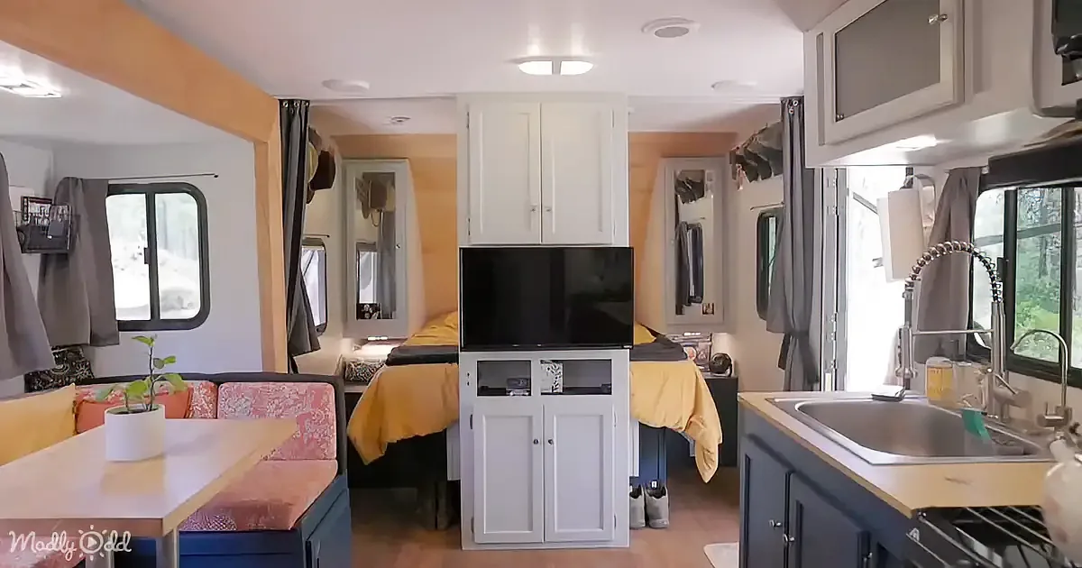 A cozy RV interior with a bed, kitchen sink, cabinets, and a TV on a stand.