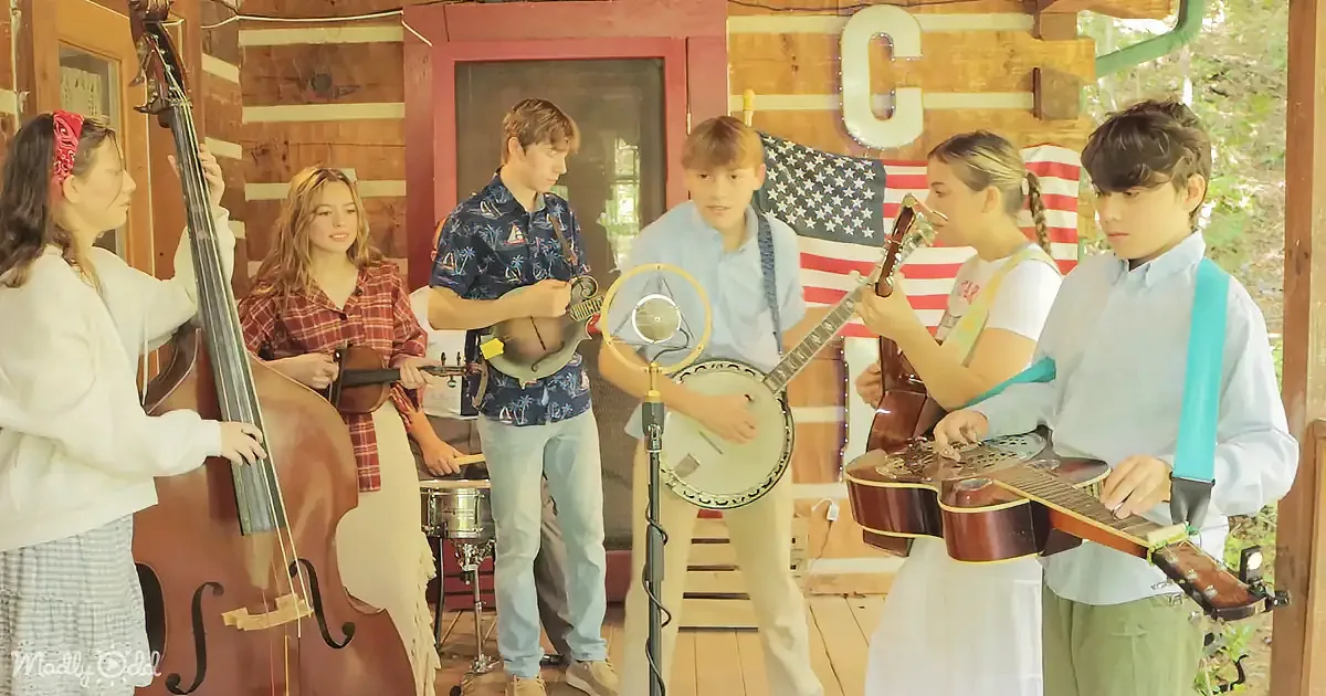 A group of young musicians plays instruments in front of a wooden backdrop with an American flag.