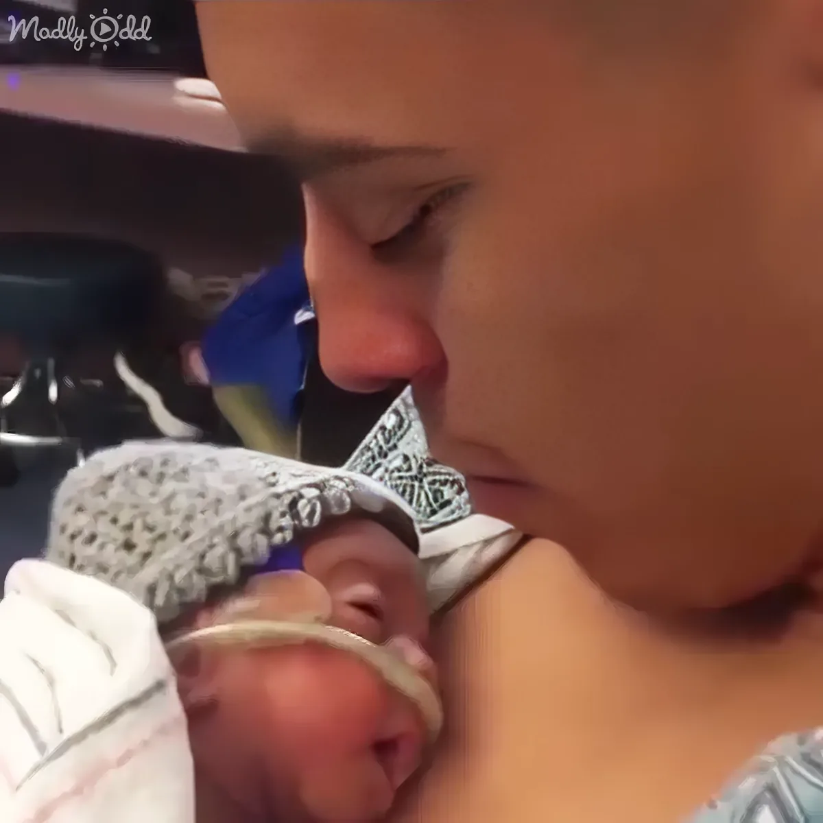 A baby wearing a knitted hat is being held and kissed by a person in a hospital setting.