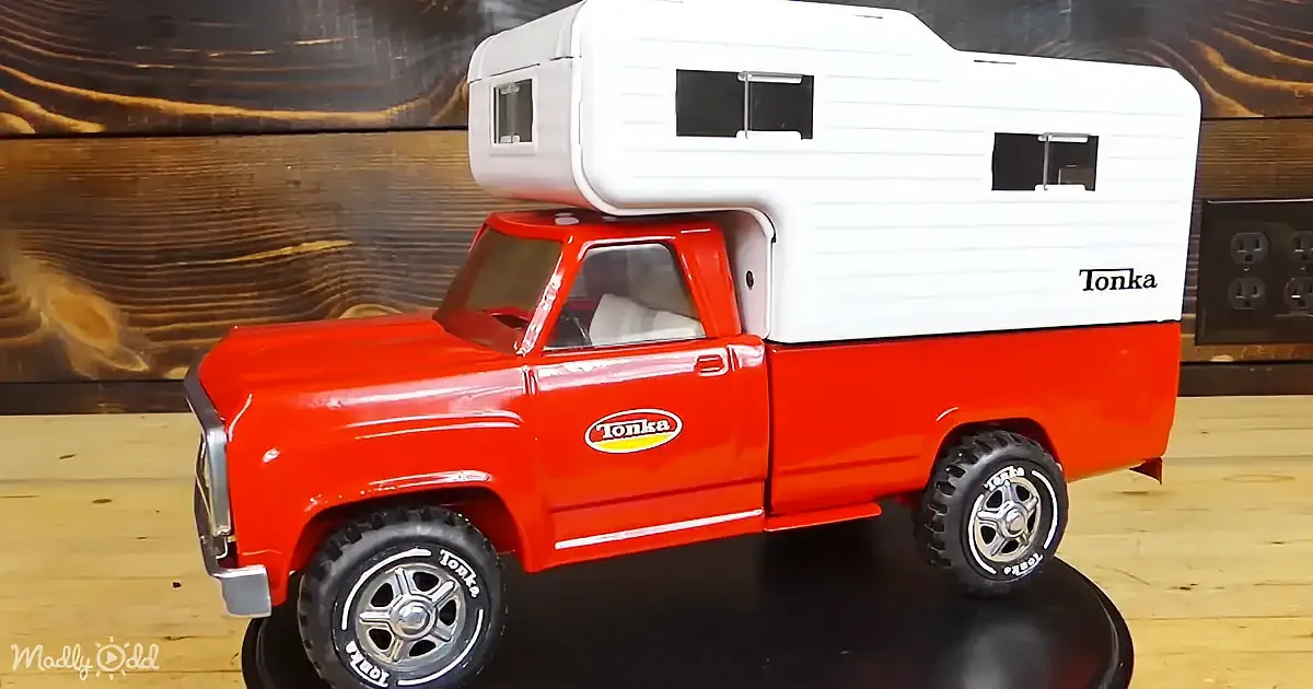 A red Tonka toy truck with a white camper on top is displayed on a wooden surface.