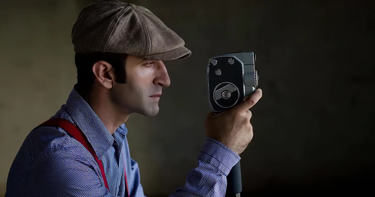 A person in a red vest holds a JVC camcorder, mouth open, with a car in the background.