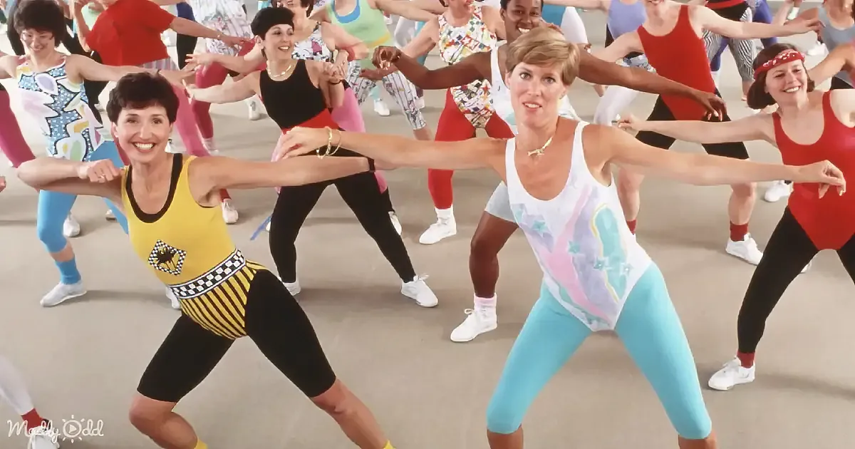 A woman in a white tank top leads a group of women in a synchronized dance workout.