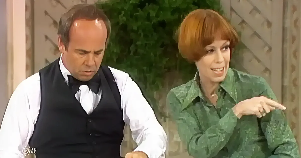 A man in a vest and bow tie looks down, while a woman in a green shirt points to the side.