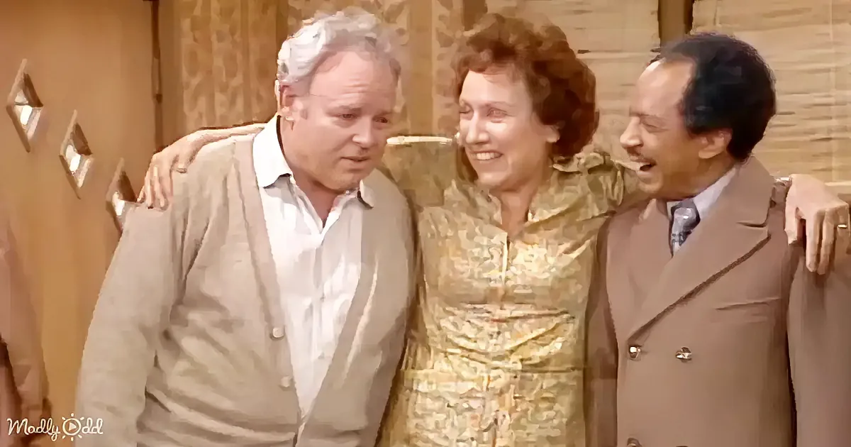 Three people, two men and a woman, are standing together, smiling and laughing, in a warmly lit room.
