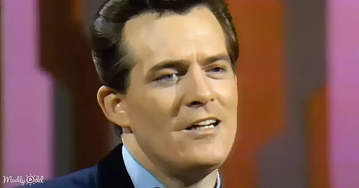 A man in a suit and tie, speaking, with a colorful background.