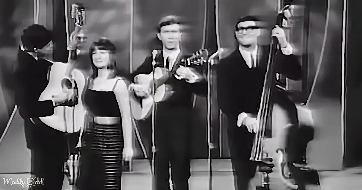 A band performs on stage, featuring a woman in a black dress and four musicians with various instruments.