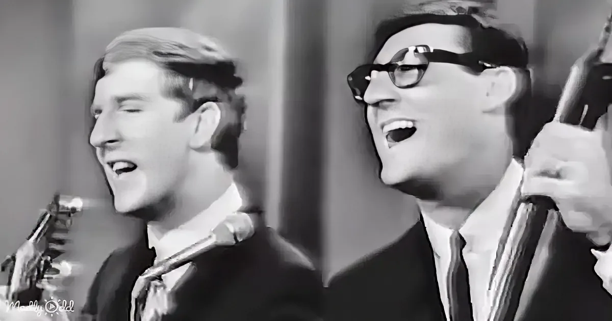 Two men in suits and ties are singing, one playing a guitar, both smiling and enjoying the performance.