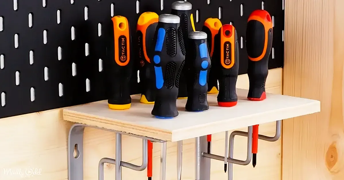 Screwdrivers with orange and black handles are neatly arranged on a wooden shelf against a pegboard wall.