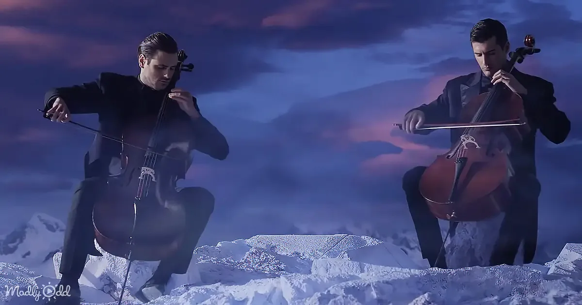 Two men in black suits play cellos on snowy ground under a twilight sky.