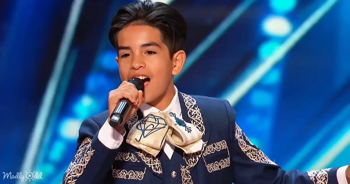 A young person in a traditional embroidered outfit sings into a microphone on stage.