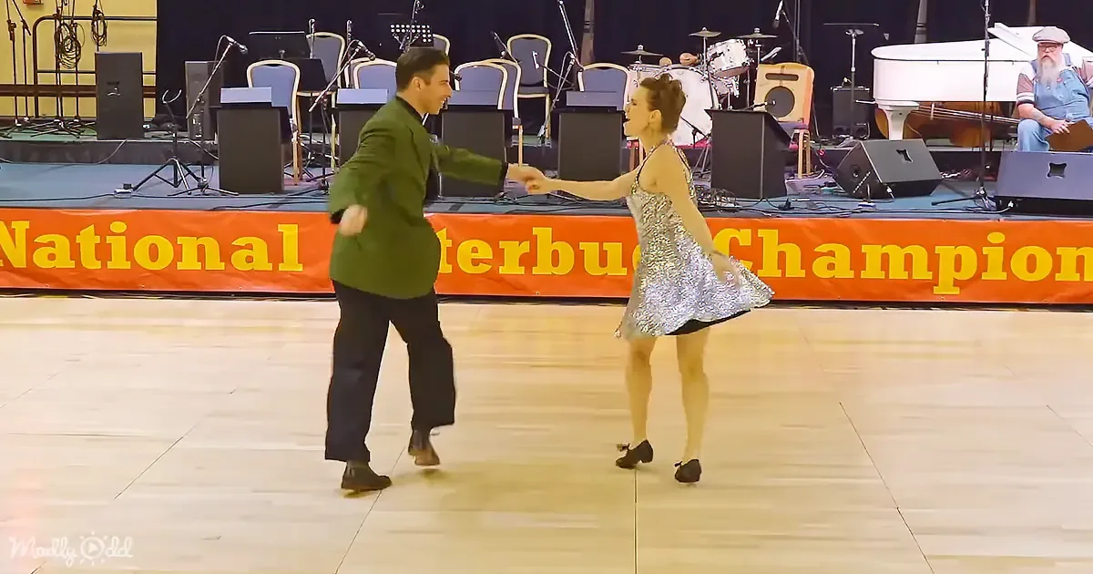 A couple dances on stage at a National Interbus Championship event, with a band and banner in the background.
