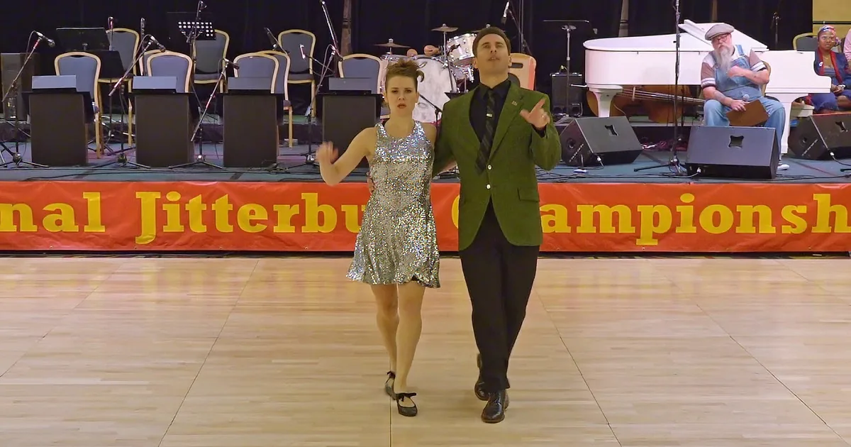 A couple dances on a wooden floor, wearing formal attire, with a banner reading "terbug Championships" in the background.