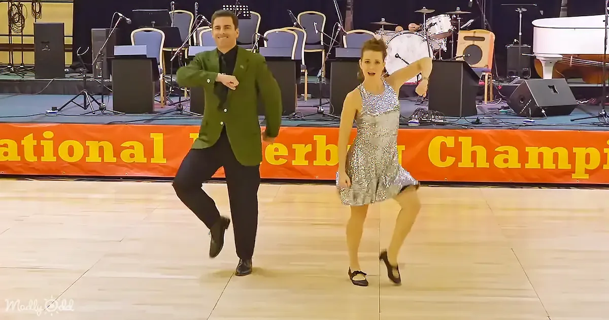 A man and woman dance on stage in front of a band setup and "National Tap Dance Championship" banner.
