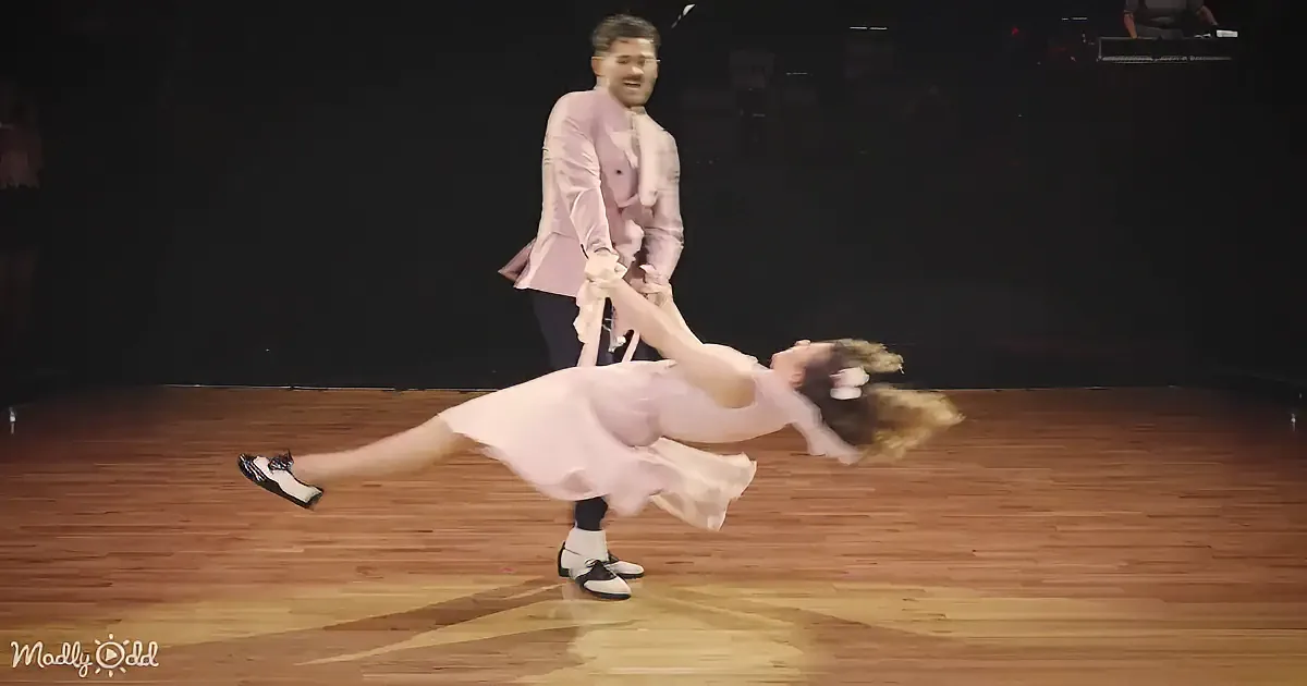 A man in a pink suit spins a woman in a pink dress on a wooden floor.
