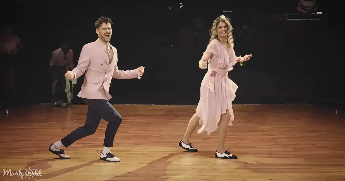 A man and woman in pink outfits dance energetically on a wooden floor.