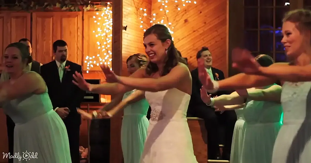 A bride in a white dress dances joyfully with bridesmaids in mint green dresses at a wedding reception.