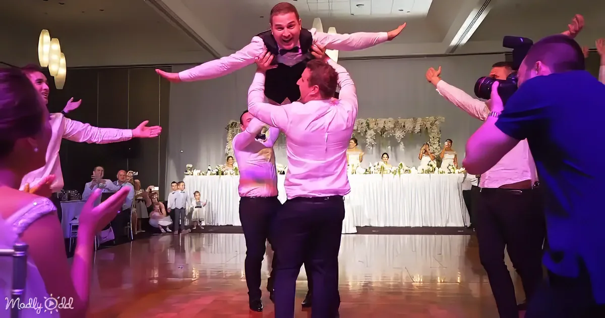A man is being lifted into the air by two others at a wedding reception.