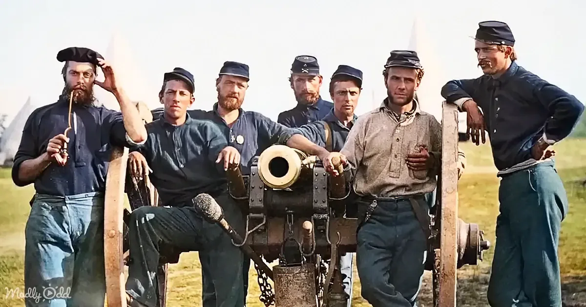 A group of men in Civil War-era uniforms pose with a cannon in a grassy field.