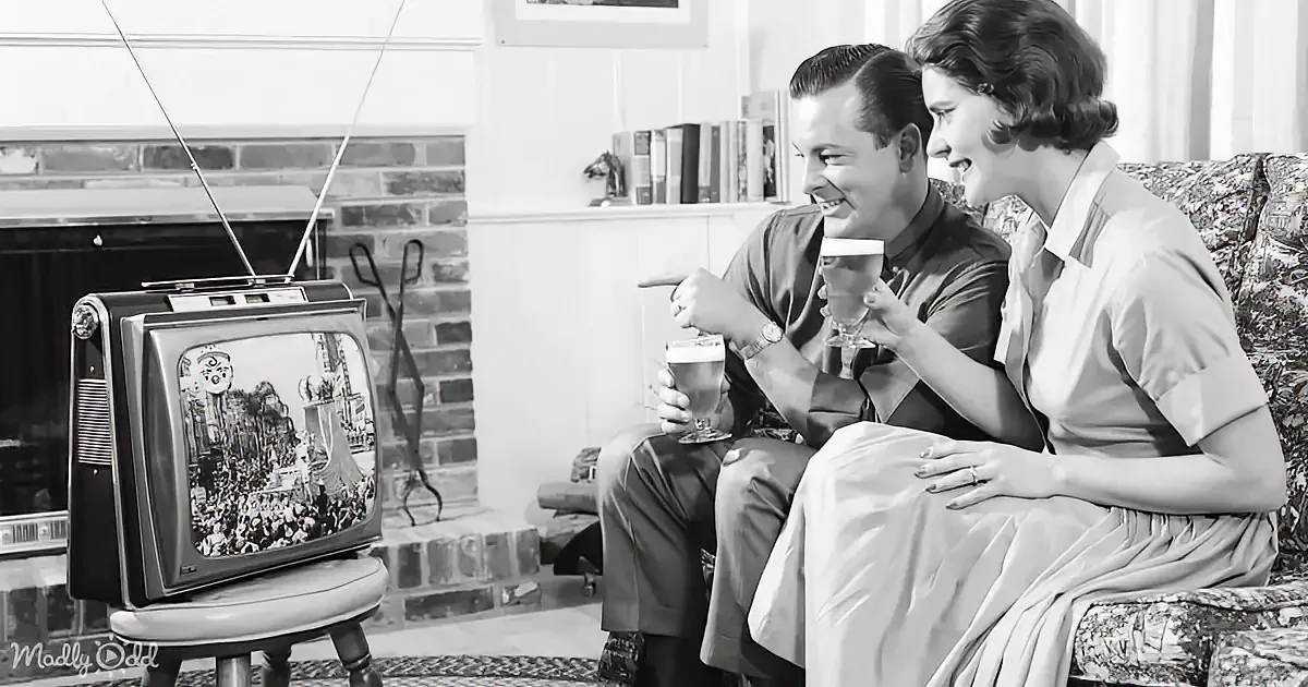 A couple enjoys a drink while watching a vintage TV in a cozy living room.