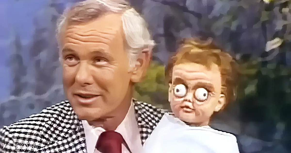 An older man in a checkered shirt and tie is holding a baby with exaggerated eyes and a surprised expression.
