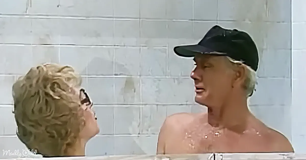A man in a cap and woman with sunglasses are in a bathtub, facing each other, with water splashing around.