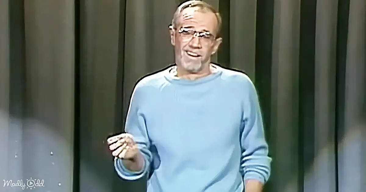 A man in a light blue sweater gestures with his right hand while speaking.