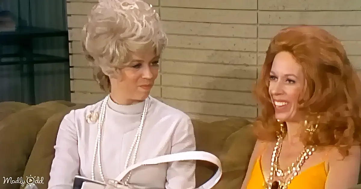 Two women are seated on a couch, one in white with pearls, the other in yellow with a smile.