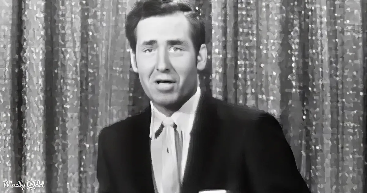 A man in a suit and tie stands in front of a glittery curtain backdrop.