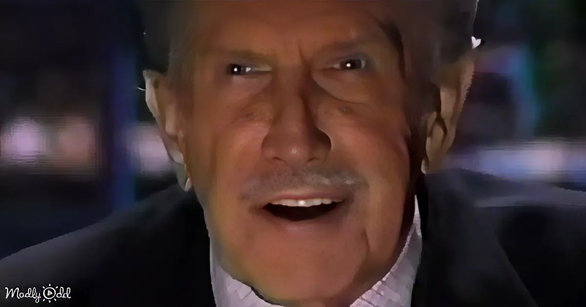 A man in a suit and striped shirt appears to be speaking or reacting, with a blurred background.
