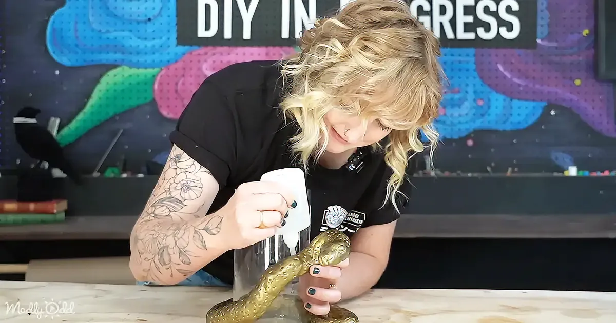 A person with tattoos and a nose ring is applying glue to a golden snake figurine.
