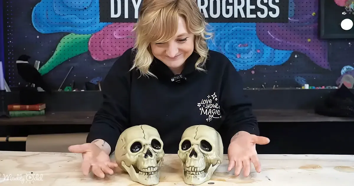 A woman in a black hoodie smiles while sitting at a table with two skull models in front of her.